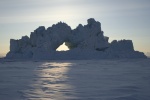 Iceberg with hole, backlit by setting sun